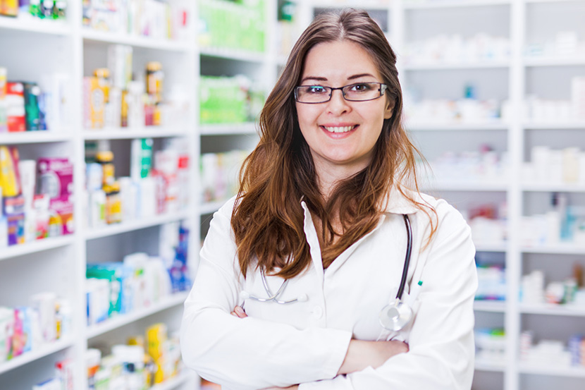 Woman in pharmacy with white coat smiling.