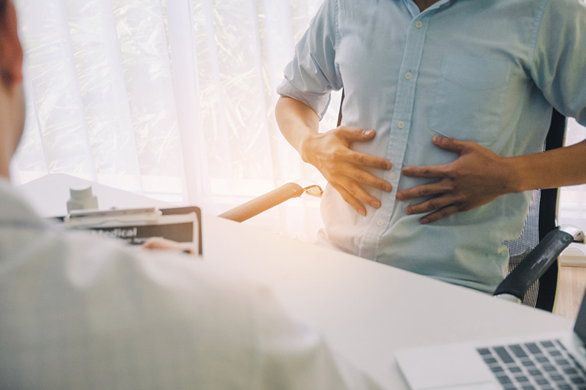 man holding stomach sitting across desk from provider